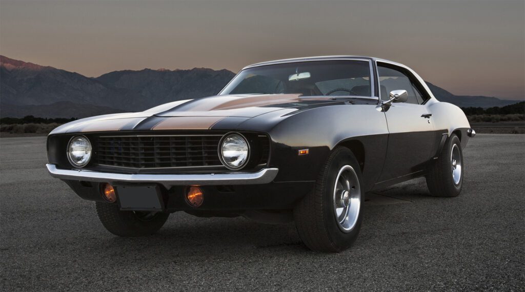Classic black muscle car parked on a road with mountains in the background.
