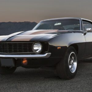 Classic black muscle car parked on a road with mountains in the background.