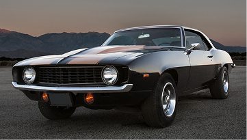 Classic black muscle car with white racing stripes parked at dusk.