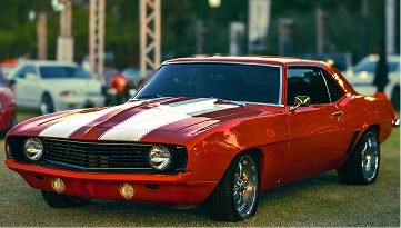 Classic red muscle car with white racing stripes parked outdoors.