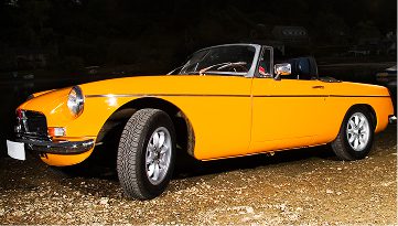 Classic yellow convertible car parked on gravel at night.